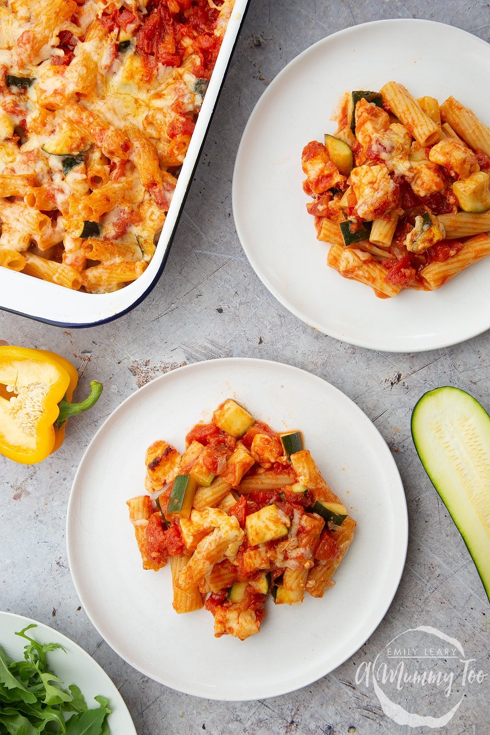 Two plates of halloumi pasta bake with the tray bake on the side. 