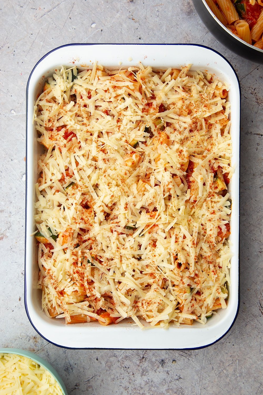 A tray of halloumi pasta bake with a sprinkle of cheese and a dash of smoked paprika on the top ready to be baked in the oven. 