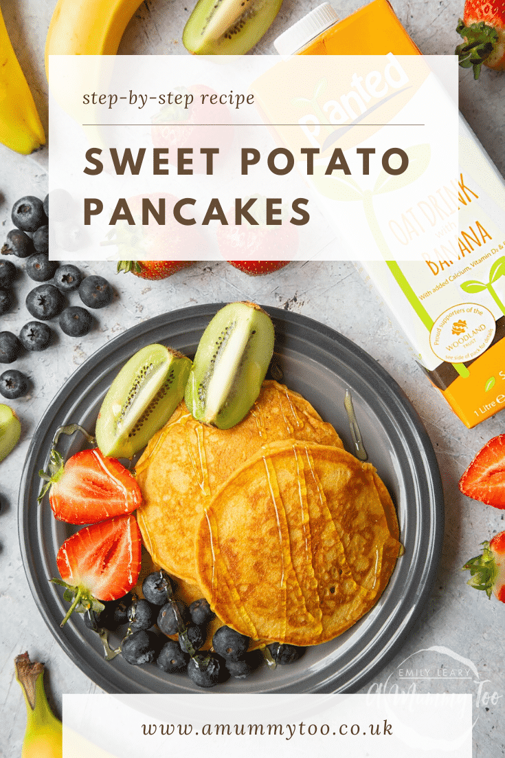 Overhead shot of two sweet potato pancakes on a black plate with a side of fruit in the form of blueberries, chopped strawberries and kiwi. The plate is surrounded by some of the ingredients used to make the pancakes.