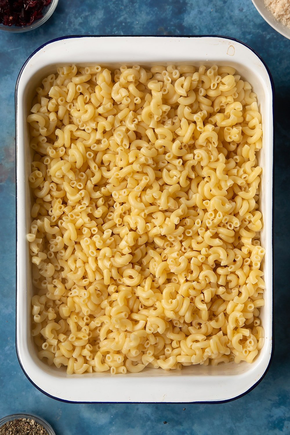 A large roasting pan filled with cooked macaroni pasta. The ingredients to make chicken and bacon mac and cheese surround the pan.