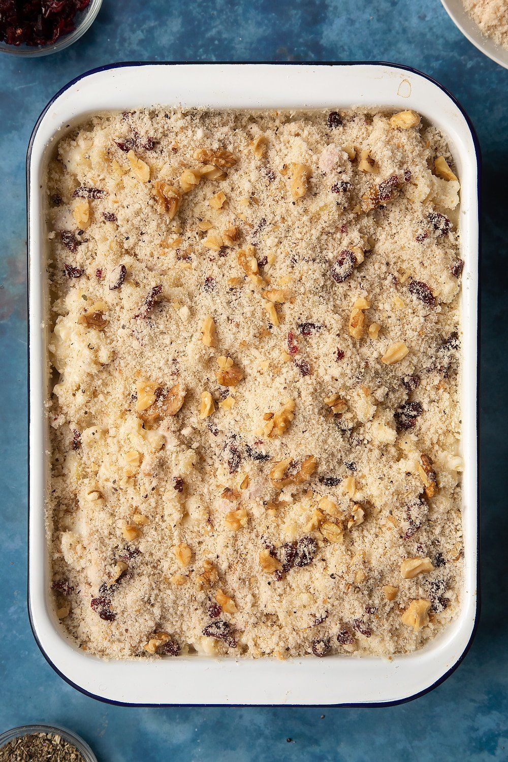 A large roasting pan filled with chicken and bacon mac and cheese, topped with a crumb made from breadcrumbs, dried cranberries, walnuts, garlic granules, dried sage, salt and pepper.