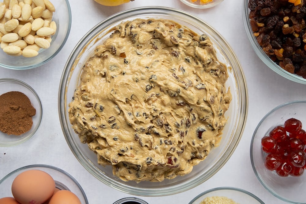 christmas fruit cake base batter mixed together in a large clear bowl surrounded by ingredients in smaller clear bowls.