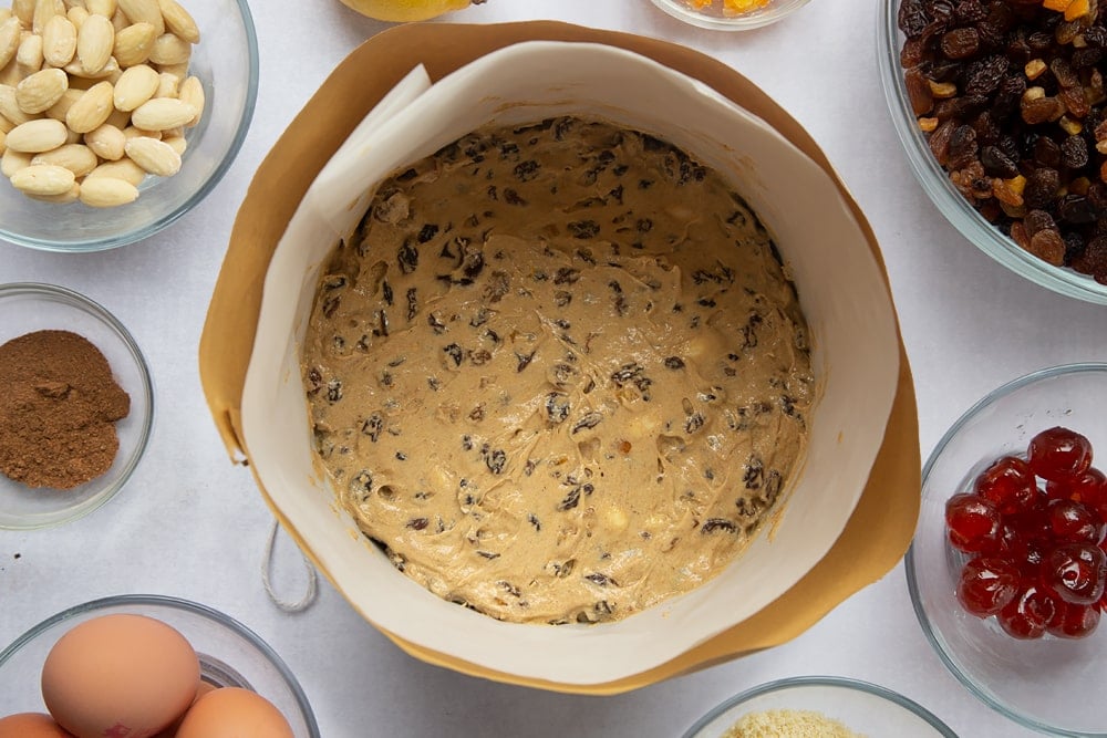 Christmas fruit cake batter in a cake tin wrapped with brown paper and greaseproof paper.