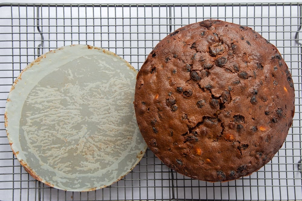 baked christmas fruit cake on a wire cooling rack with the base greaseproof paper removed.