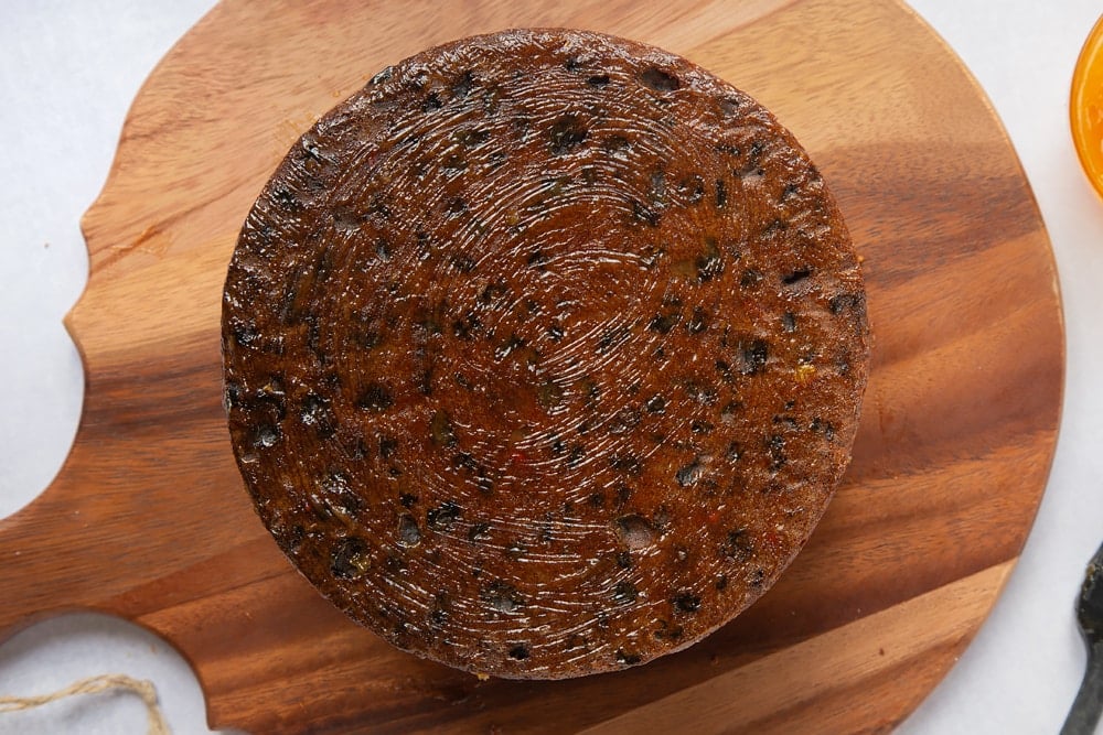 a christmas fruit cake baked laid on a round wooden chopping board with apricot jam spread on the base.