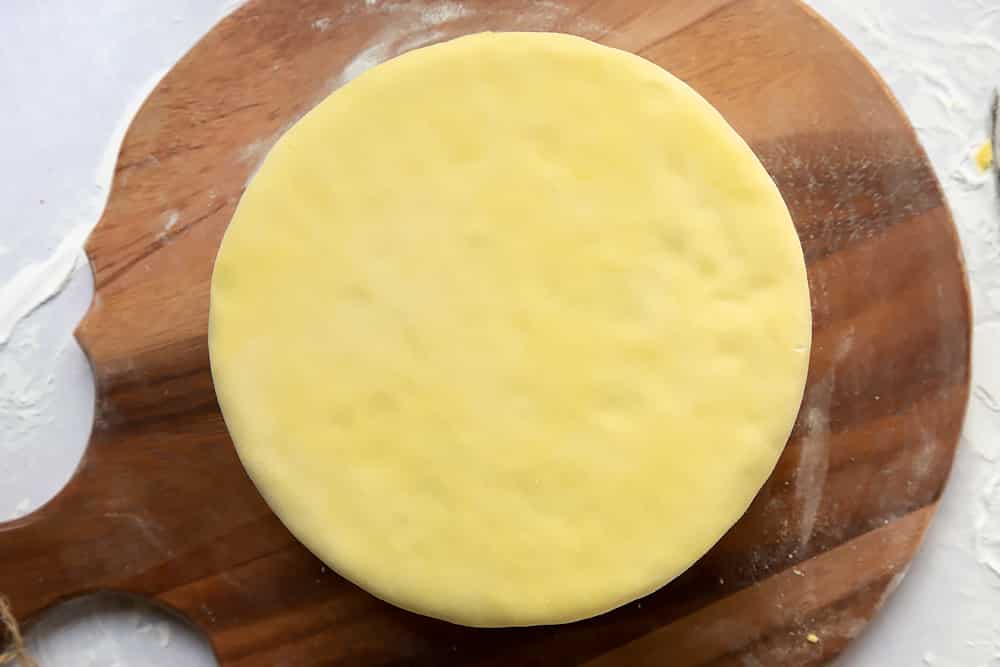 a thin layer of marzipan covering a fruit cake sat on a round wooden chopping board.