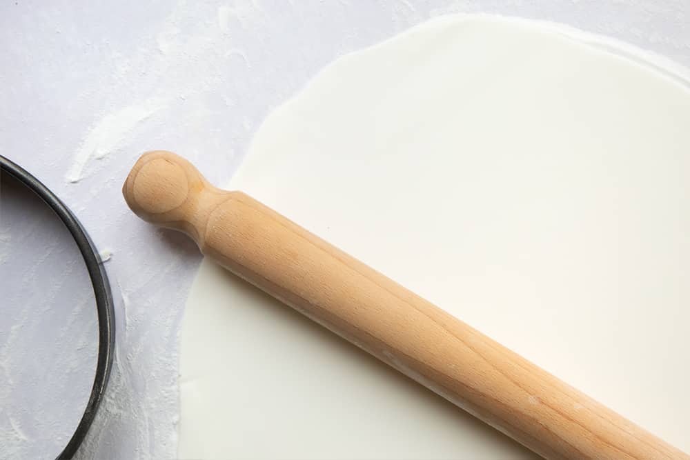 a thin layer of sugar paste rolled out on a floured surface with a cutter and rolling pin on the side.
