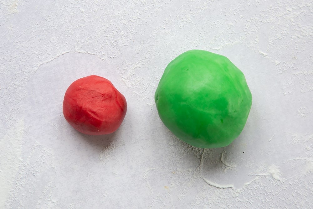 one small red ball of sugar paste and one large green ball of sugar paste on a floured surface.