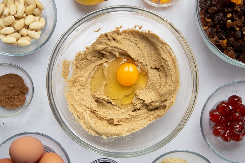 brown sugar, butter mix creamed together topped with an egg in a large clear bowl surrounded by ingredients in smaller clear bowls.