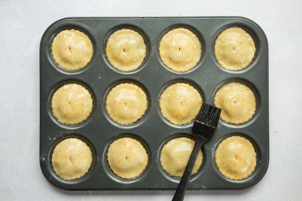 Mince pies brushed with egg whites for glaze situated in a tin.