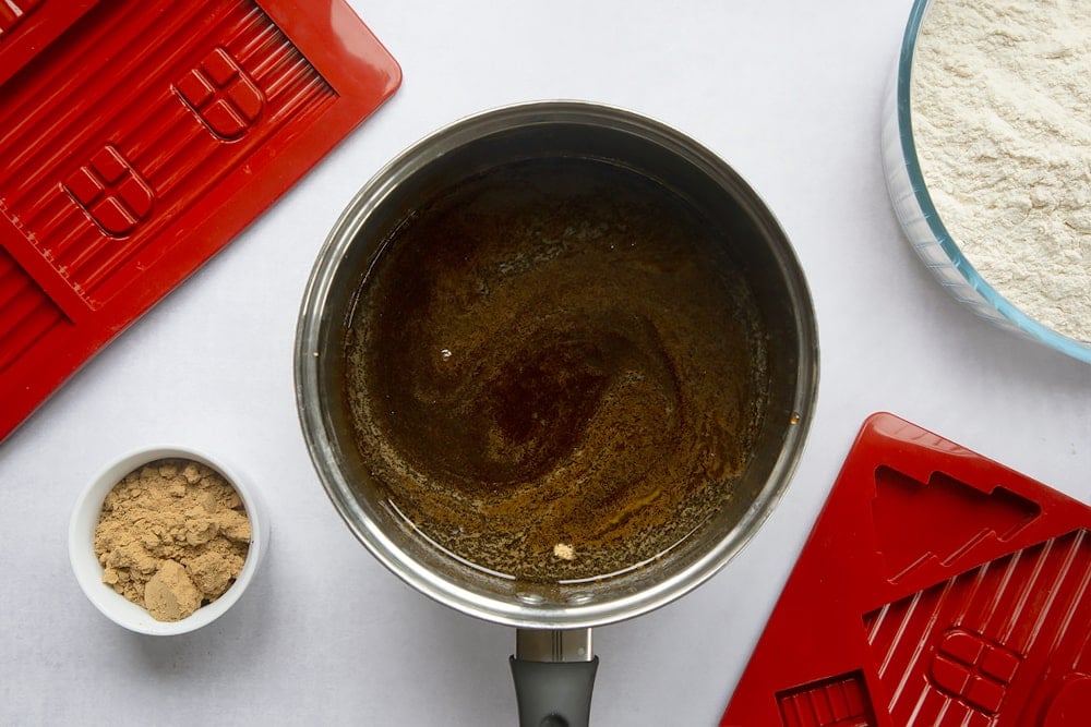 A saucepan, surrounded by equipment to make a gingerbread house. In the pan is a dark brown syrup, made from melted butter, sugar, black treacle and golden syrup.
