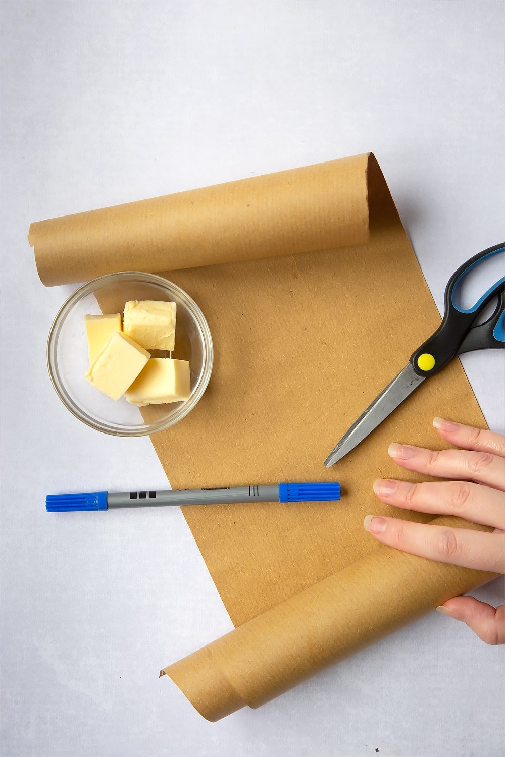 a hand holding a scroll of brown paper with a pair of scissors and pen.