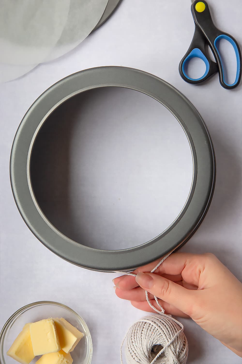 Measuring the inner lining of the cake tin using string (non-plastic) which will be cut using the scissors displayed at the side of the image. 