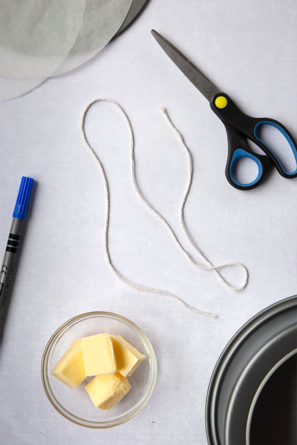 Adding an additional 5cm to the measurement of the string before cutting. Image depicts a cut string with decoration of scissors and a pen. 