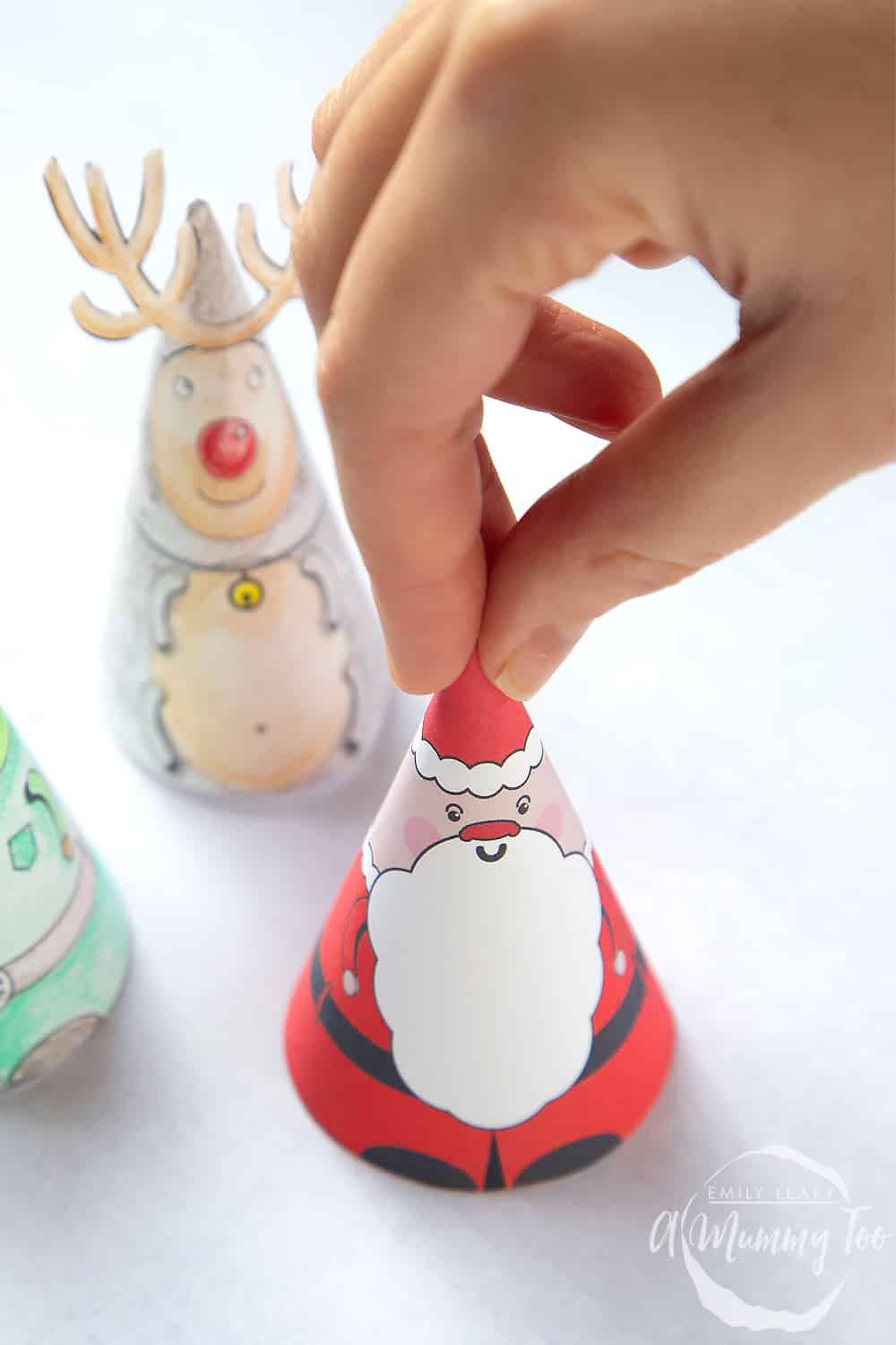 a hand holding a pyramid santa decoration with an elf and reindeer in the background.