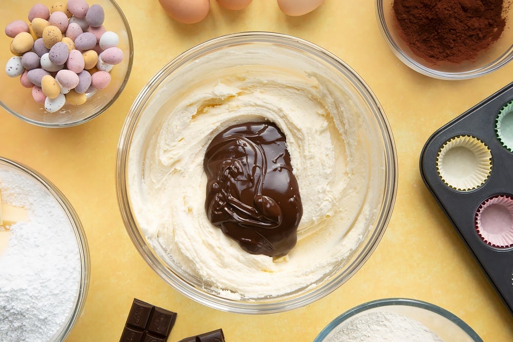 Overhead shot of frosting with melted dark chocolate in a large clear bowl