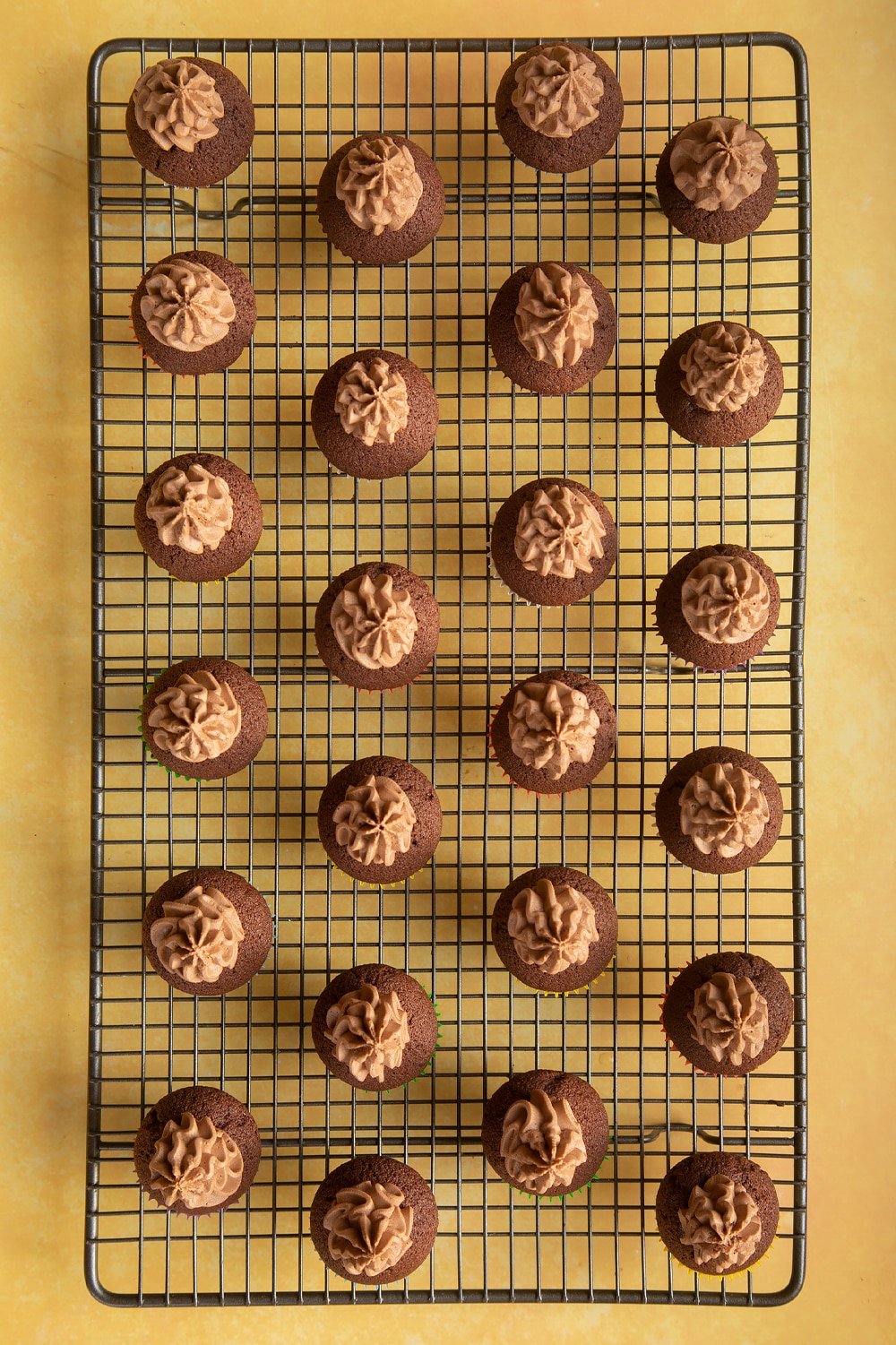 Overhead shot of chocolate muffins topped with chocolate frosting on a baking rack 