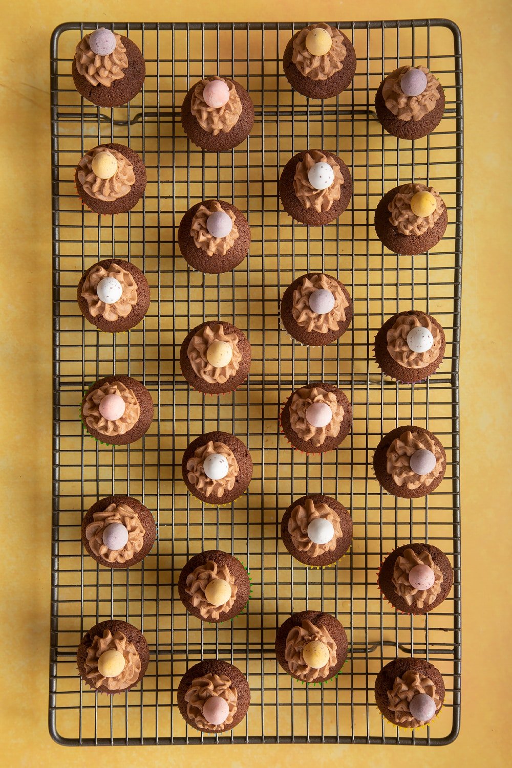 Overhead shot of chocolate muffins topped with chocolate frosting and mini chocolate egg on a baking rack 