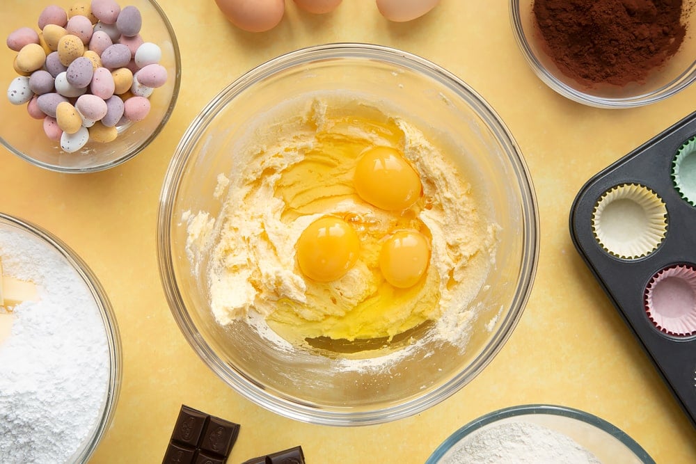 Overhead shot of margarine mix and three eggs in a large clear bowl