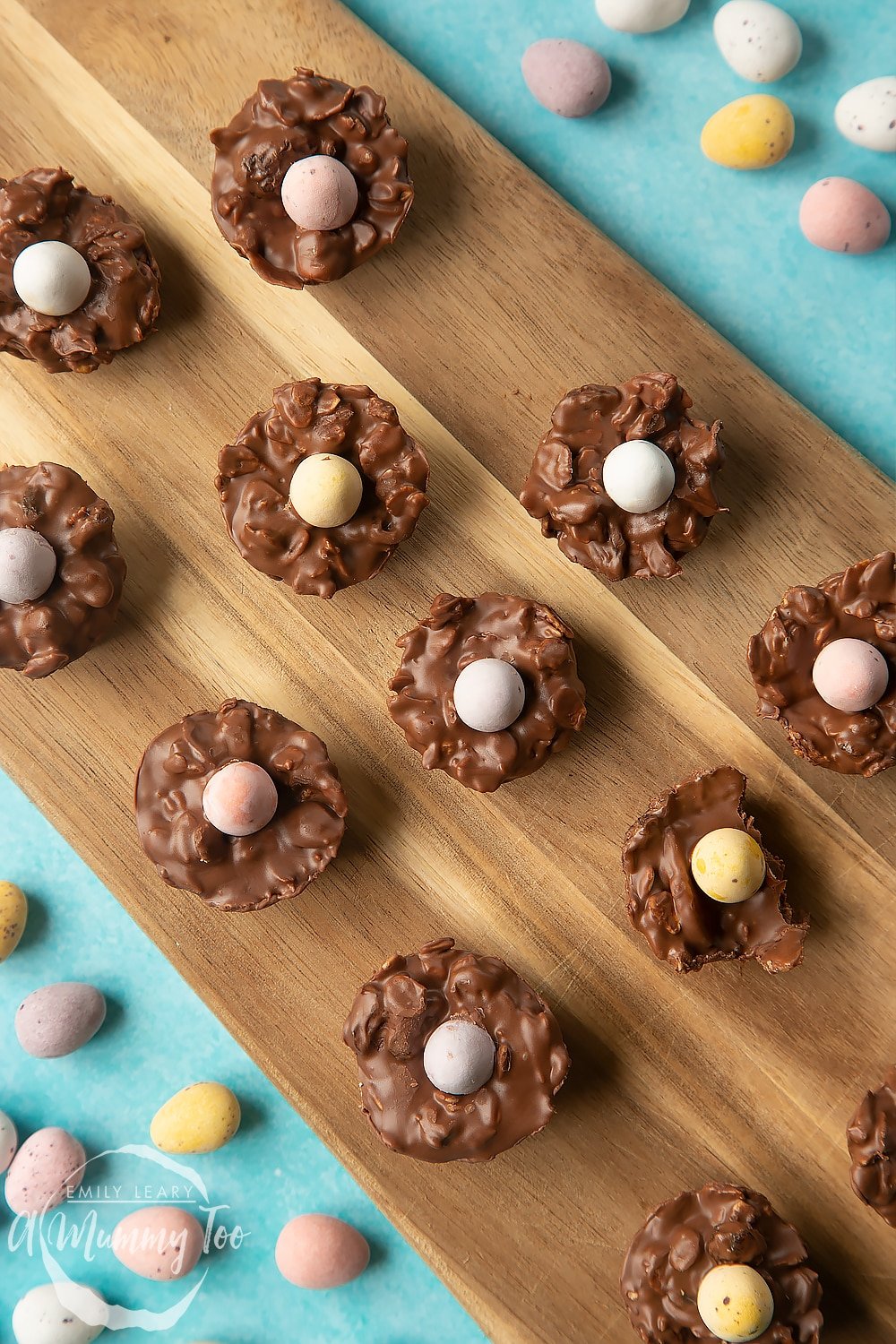  Overhead shot of a hand holding a chocolate Easter nest cakes on a wooden board.