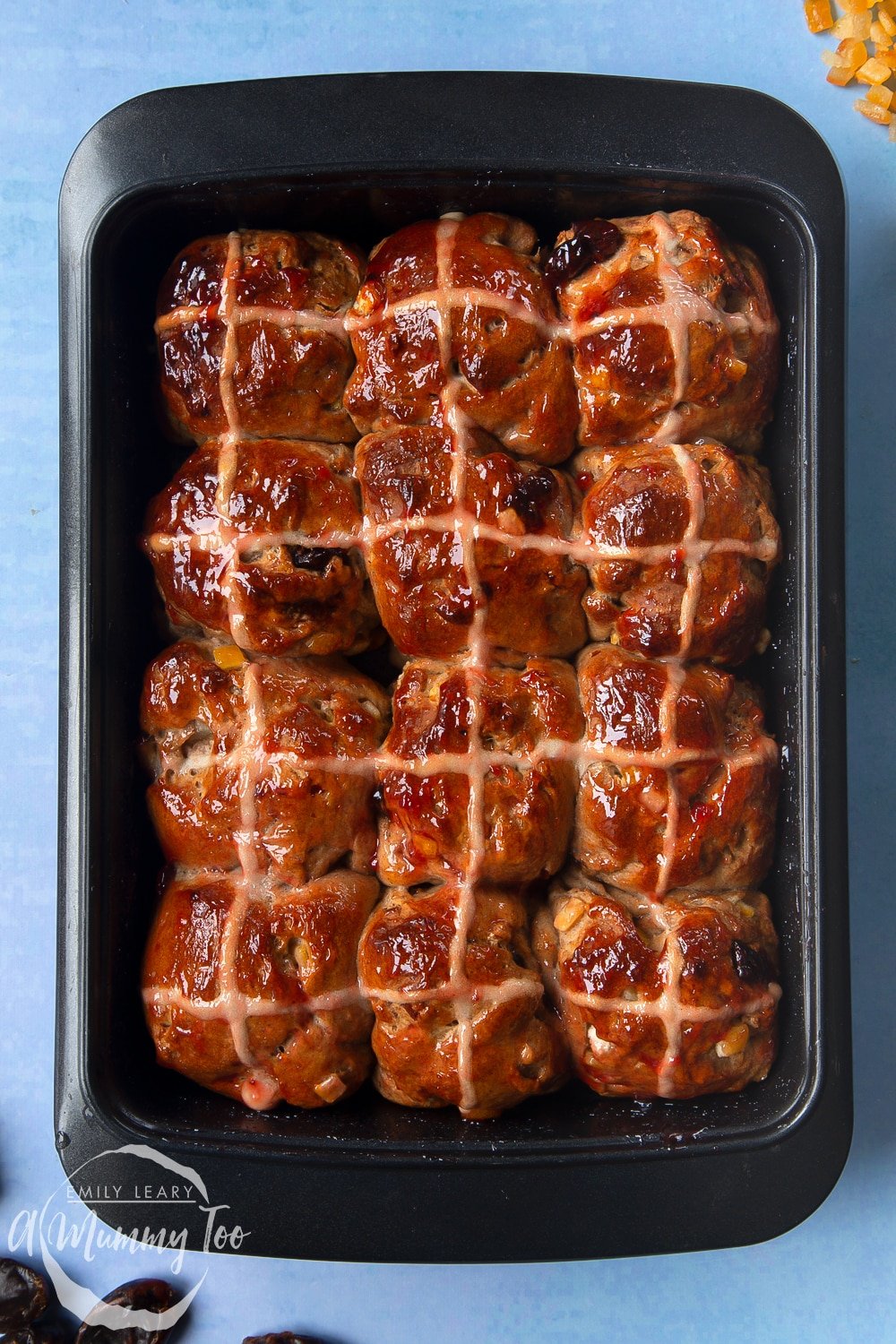 Freshly baked vegan hot cross buns in a baking tray, brushed with jam.