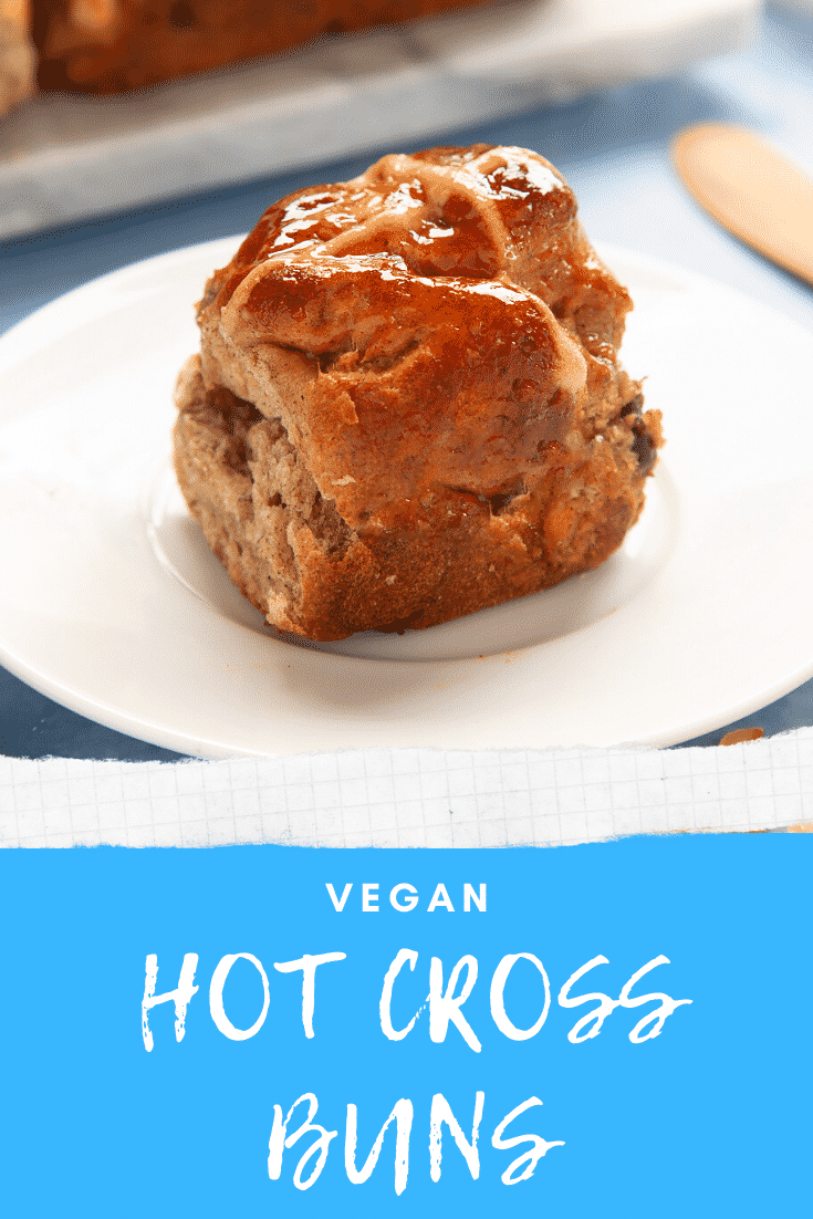 A freshly baked vegan hot cross bun on a white plate. Caption reads: vegan hot cross buns