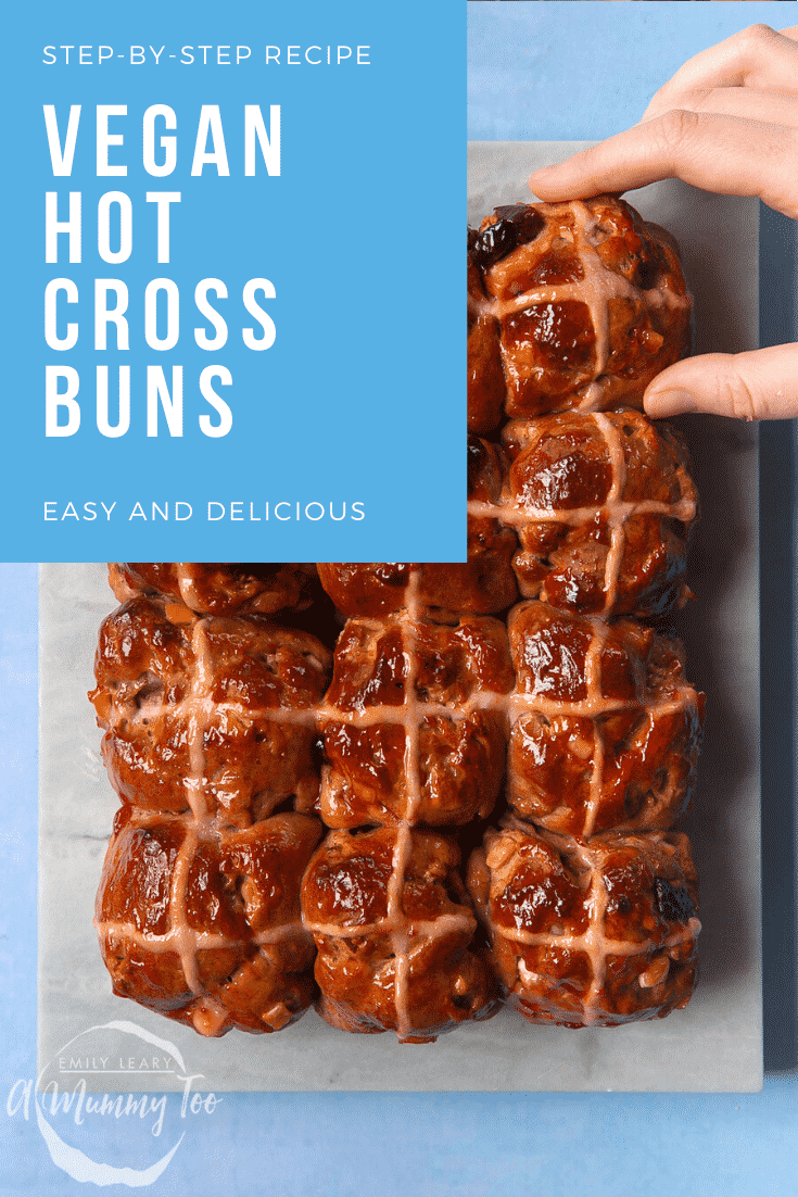 12 vegan hot cross buns on a marble board. A hand reaches in as if to take one. A caption reads: step-by-step recipe - vegan hot cross buns - easy and delicious