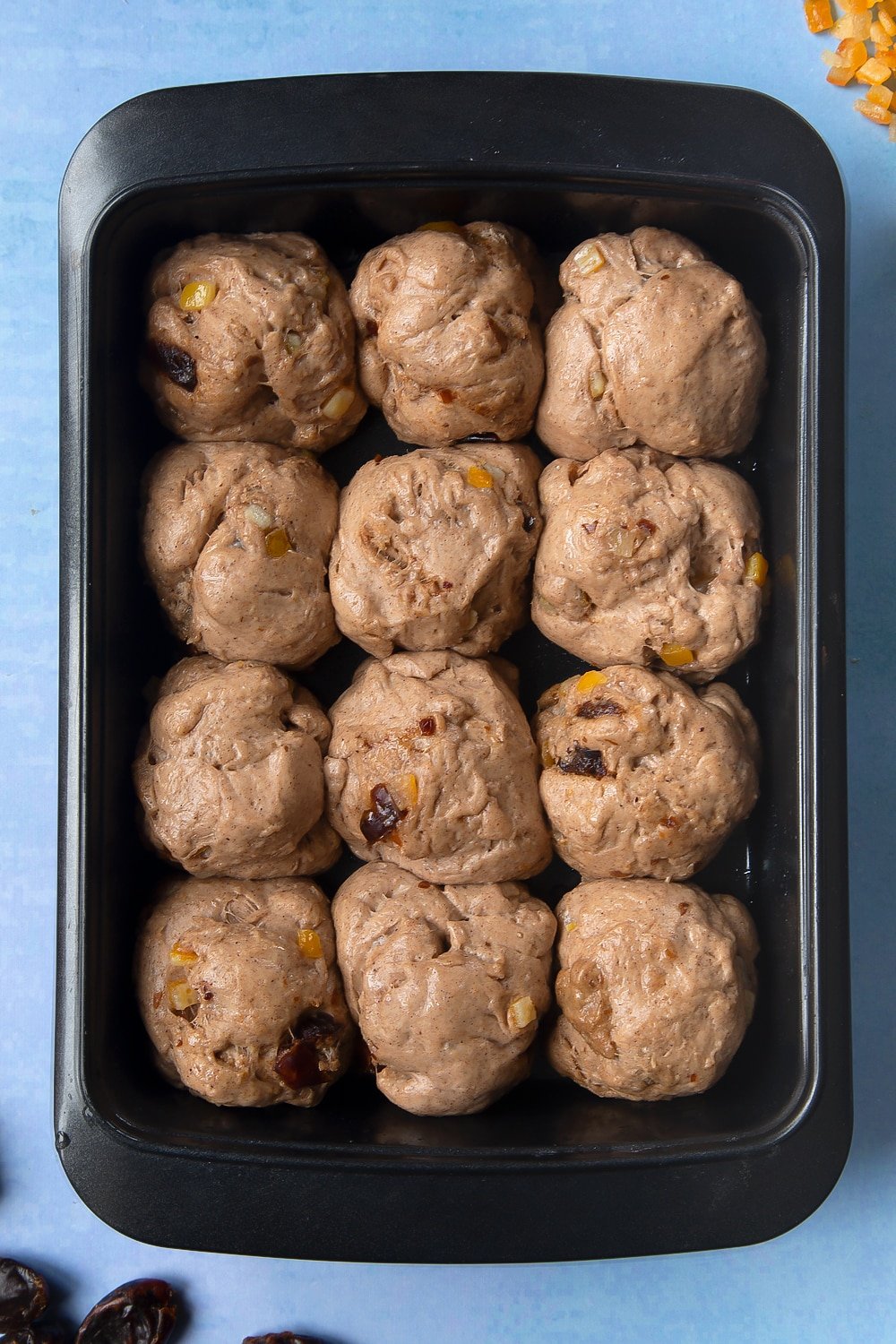 Vegan hot cross buns dough with mixed peel and chopped dates, divided into 12 balls and proved in an oiled tray.