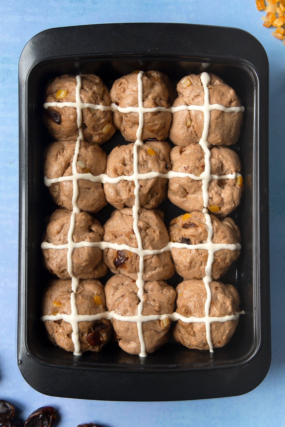 Vegan hot cross buns dough divided into 12 balls and proved in an oiled tray. Thin lines of flour and water paste are piped across the buns 