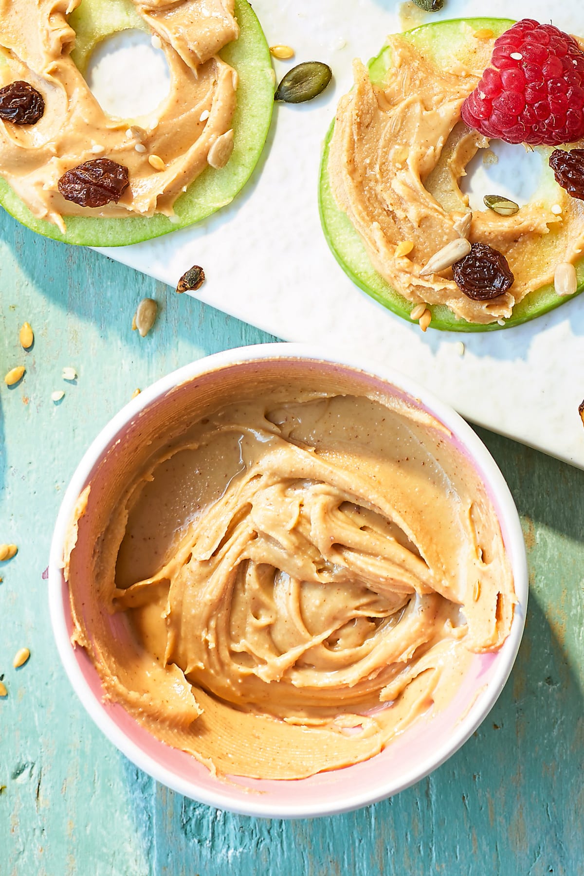 Peanut butter in a pink bowl, next to a white board topped with apple slices with peanut butter.