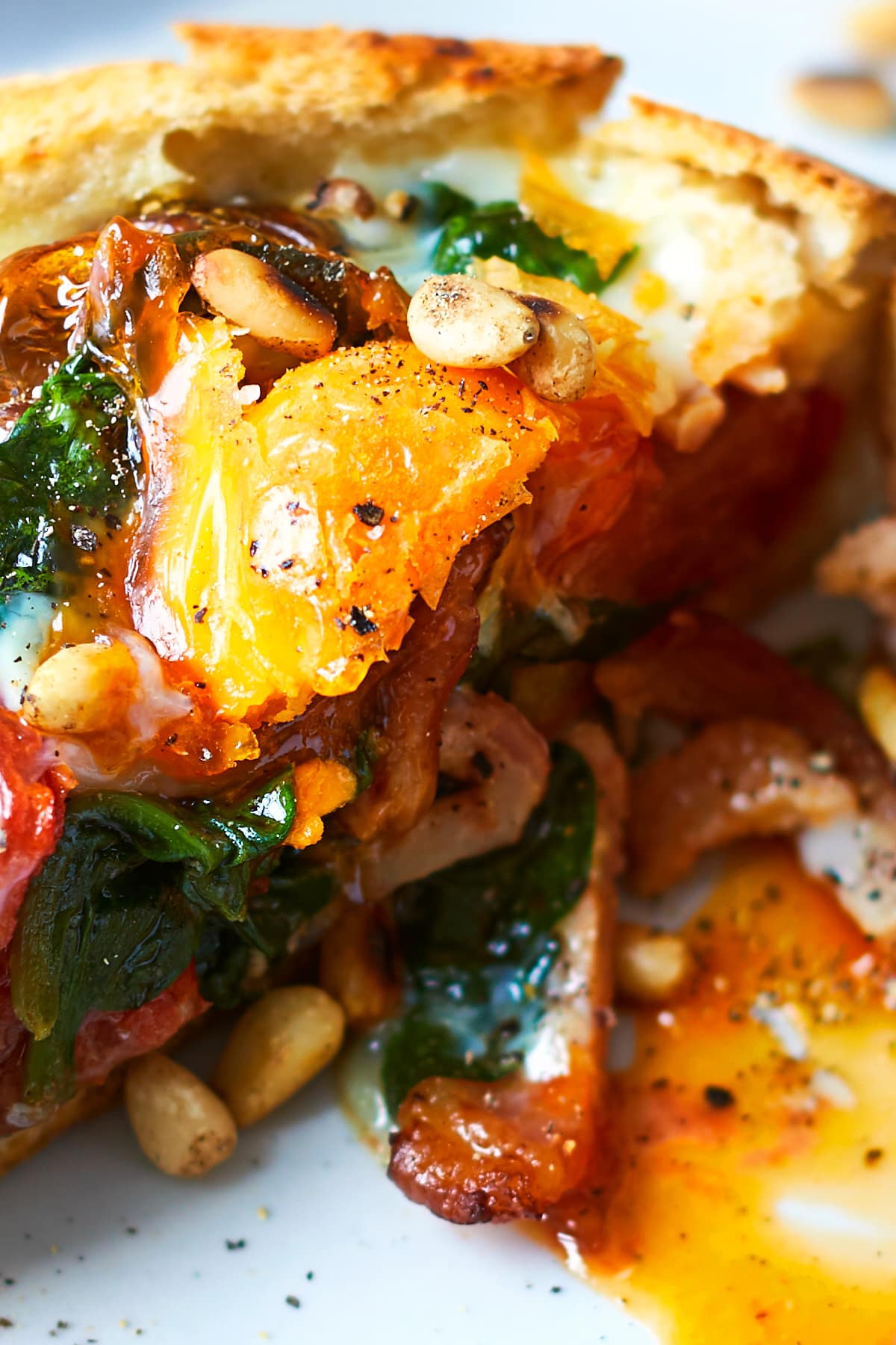 A close up of a breakfast roll, filled with sausage, bacon, spinach, tomatoes and pine nuts, topped with an egg. The roll is cut open to reveal the runny egg yolk.