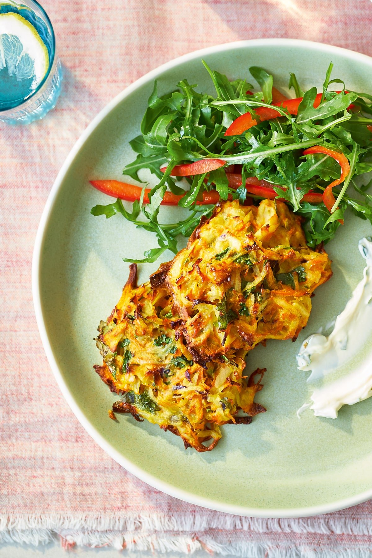Two carrot patties on a green plate with a rocket and pepper salad.