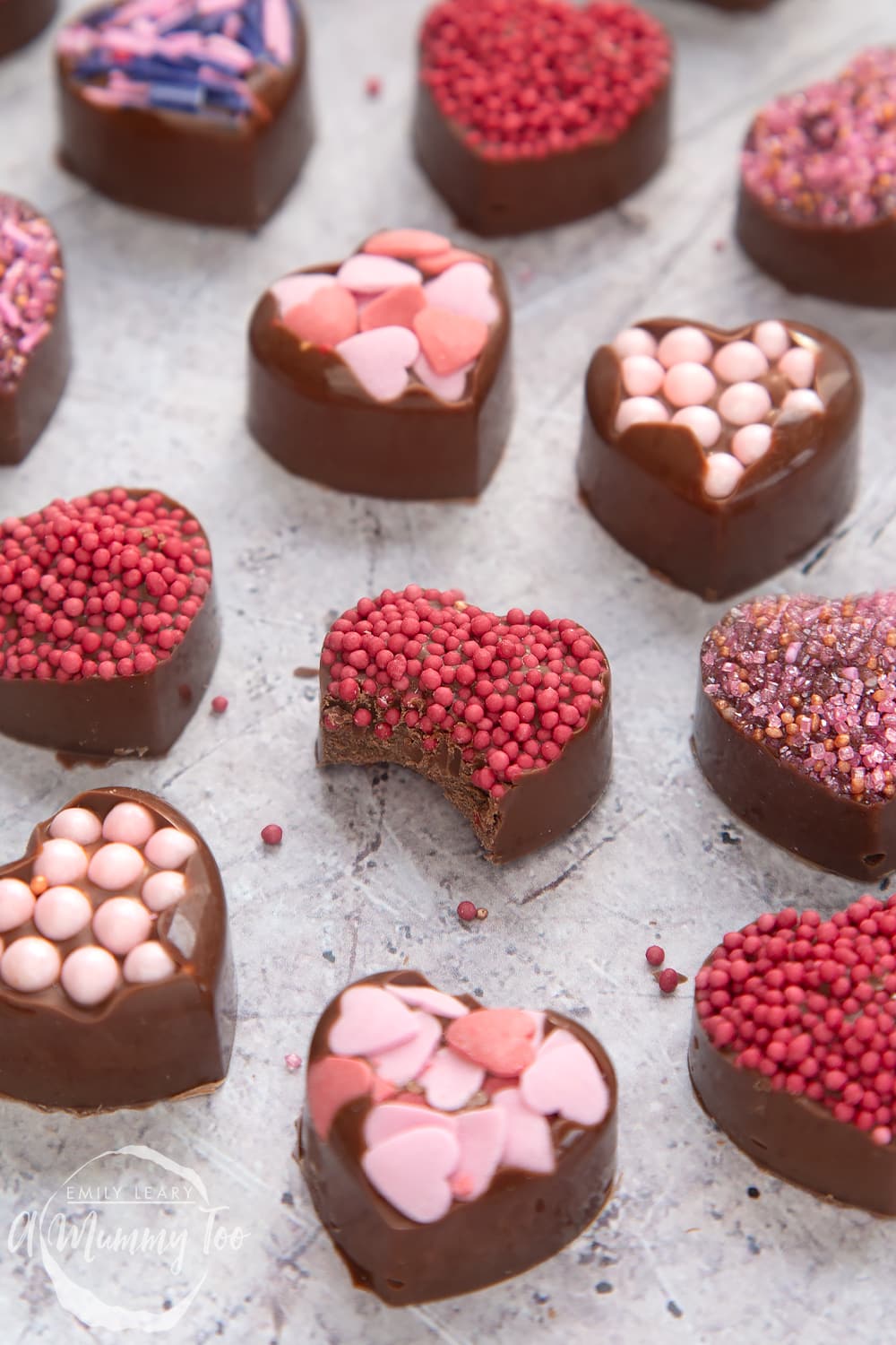 front angle shot of a half eaten chocolate heart with pink sprinkles with a mummy too logo in the lower-left corner