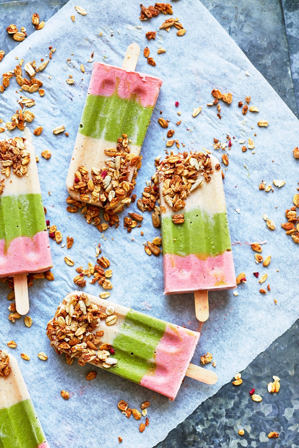 Fruit and veg lollies arranged on a granite board. The lollies have been dipped in granola.