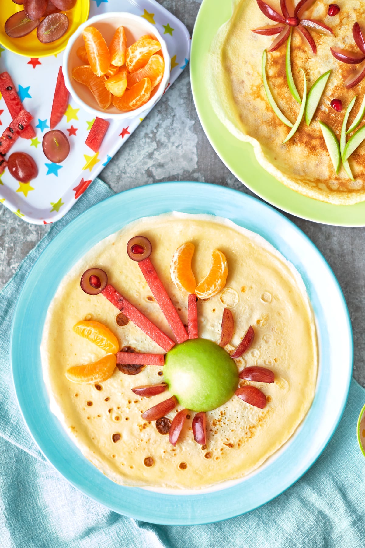 A crepe-style pancake on a blue plate is decorated with fruit to resemble a crab.
