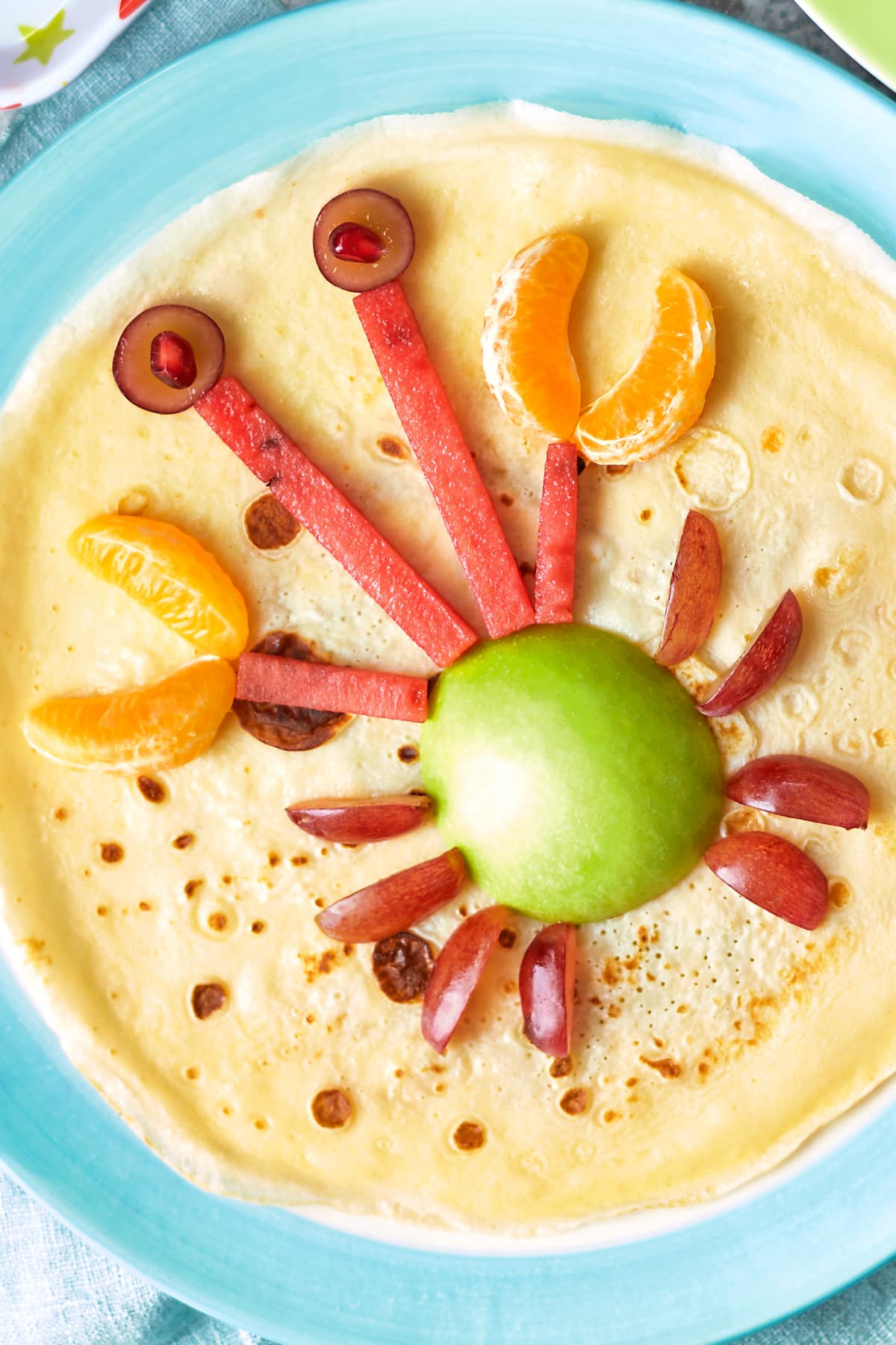 A crepe-style pancake is decorated with fruit to resemble a crab.