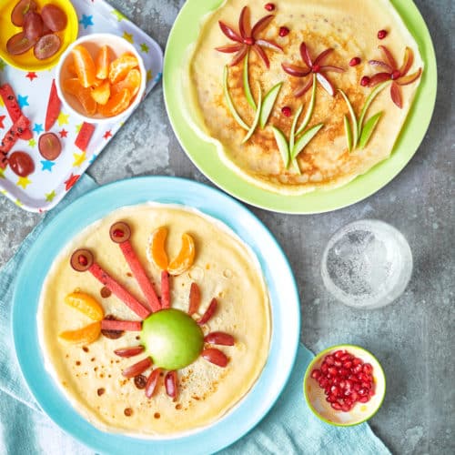 overhead view of 2 plates with crepe like pancakes with a crab and flower designs made out of vegetables.