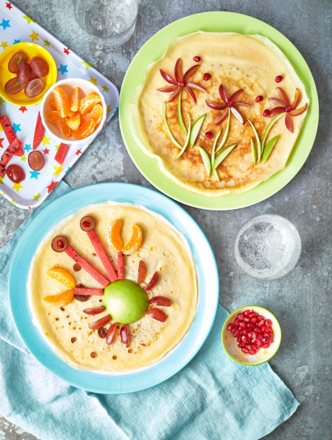 overhead view of 2 plates with crepe like pancakes with a crab and flower designs made out of vegetables.