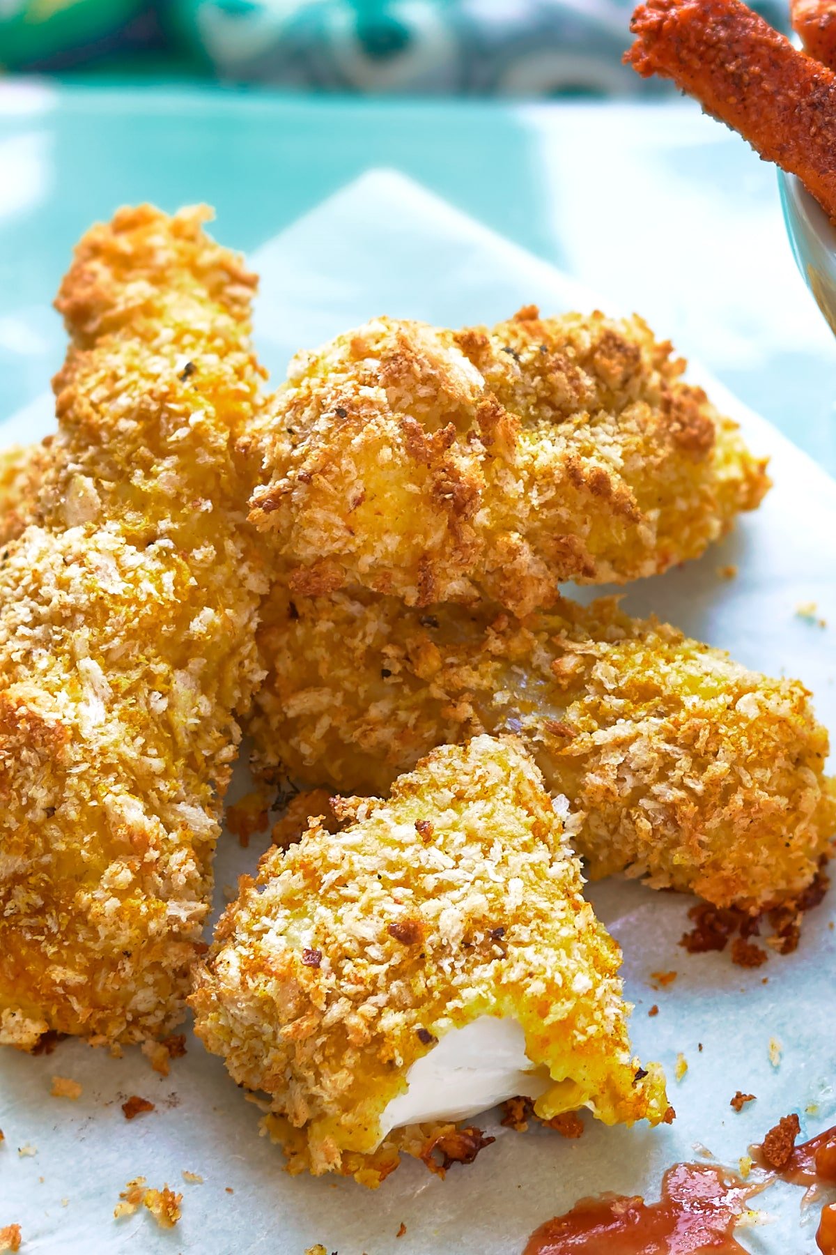 Close up of homemade spicy fish sticks on a sheet of paper on a pale blue tray.