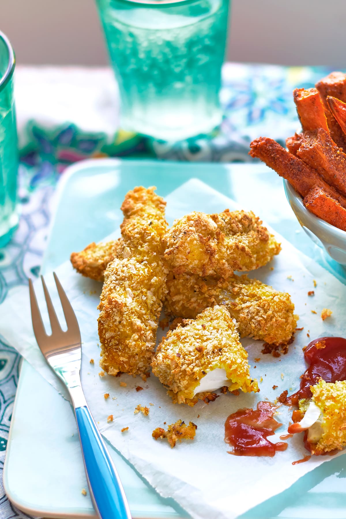 Homemade spicy fish sticks on a sheet of paper on a pale blue tray. 