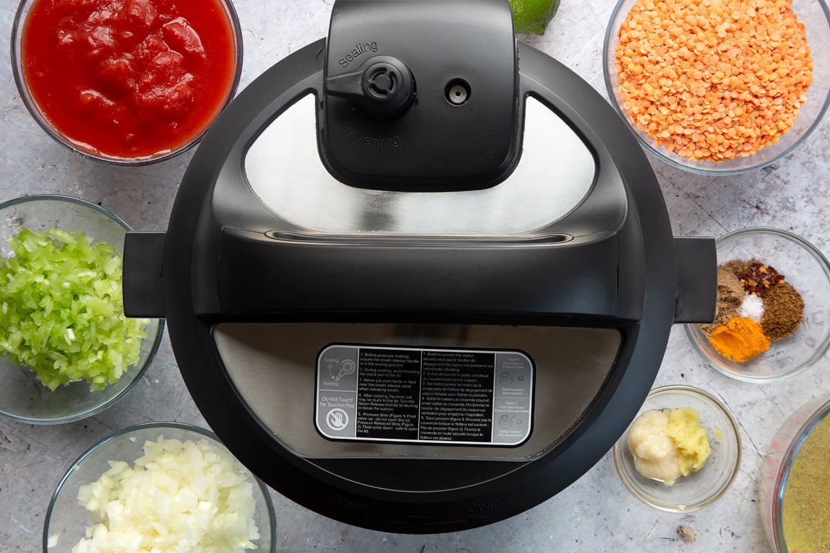 Overhead shot of slow cooker with its lid on surrounded by ingredients in clear bowls