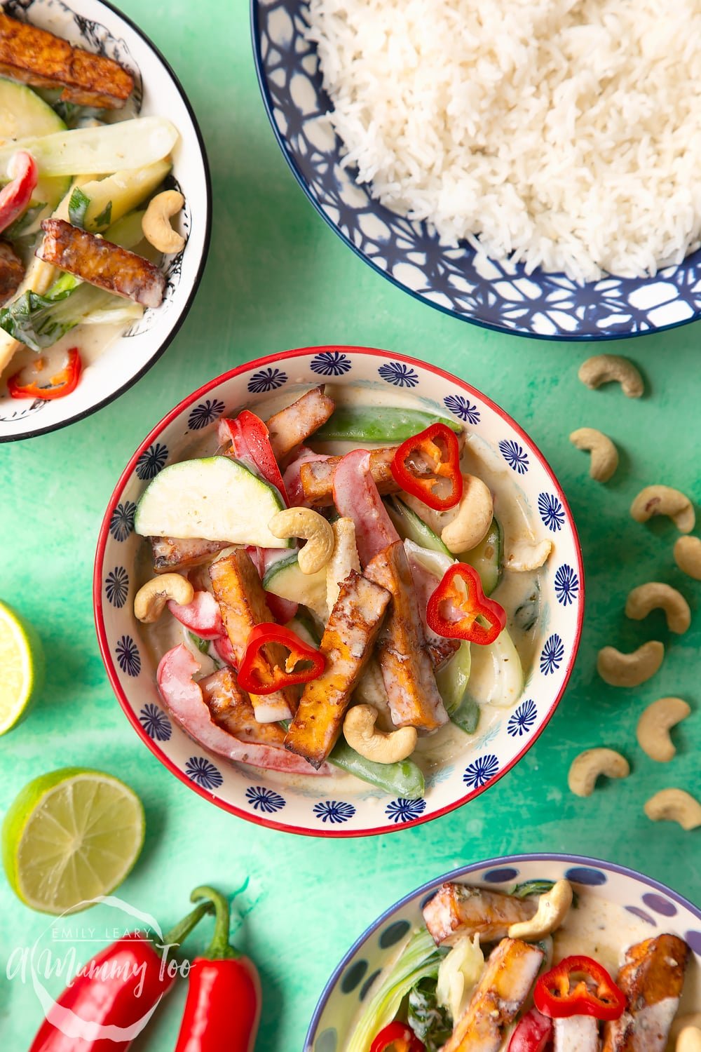 an overhead view of a bowl of Thai green curry in a decorative blue and red bowl with cashew nuts strewn around the edges.