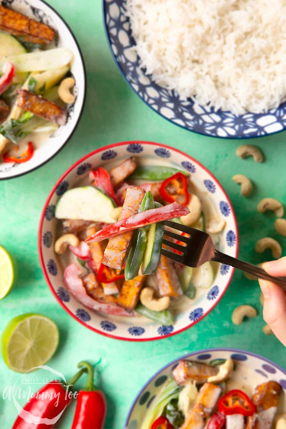 thai green curry in a small decorative bowl on a green background with a fork at teh forefront holding tofu, peppers and courgette.