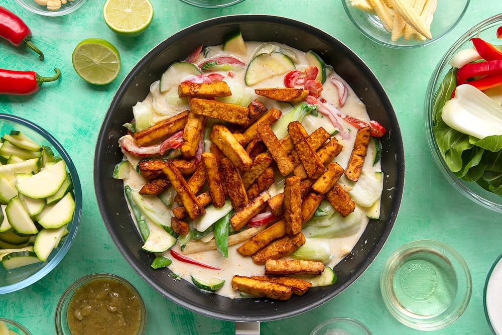 a black wok filled with bok choi, sweetcorn, red pepper, bamboo, sugar snap peas and courgette in a yogurt curry sauce topped with fried tofu.