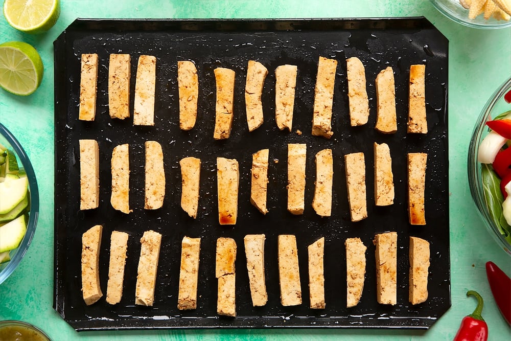 strips of soy sauce coated tofu laid out on a baking tray evely spaced.