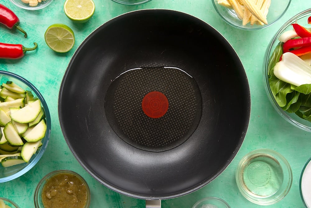 a black wok frying pan with oil in the bottom with glass mixing bowls of vegetables around the edges.