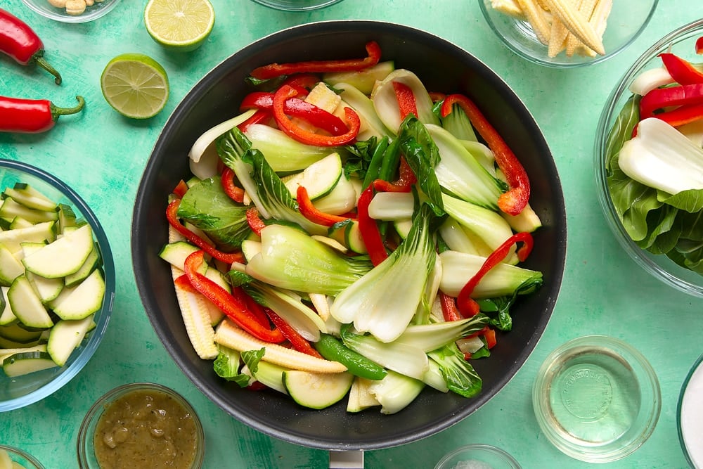 a black wok filled with bok choi, sweetcorn, red pepper, bamboo, sugar snap peas and courgette