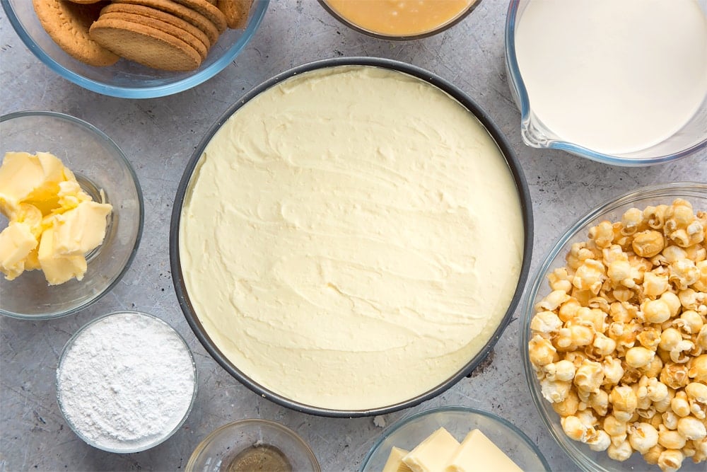 frozen cheesecake base topped with caramel and whipped cheesecake mixture in a cake tin.