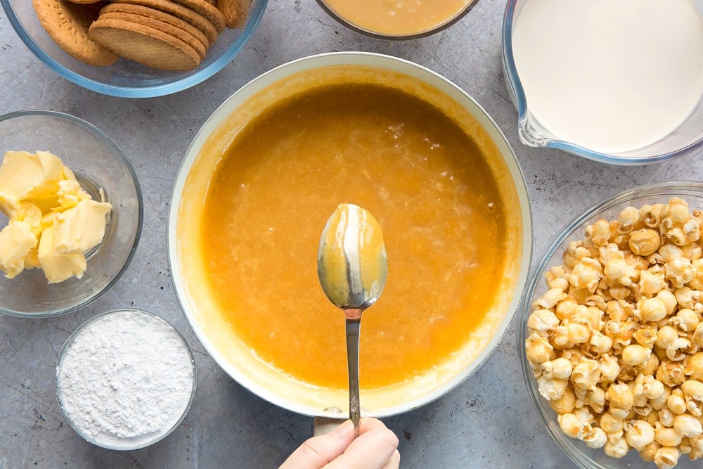 overhead view of creamy caramel sauce in a saucepan with a hand holding a spoon over the top.