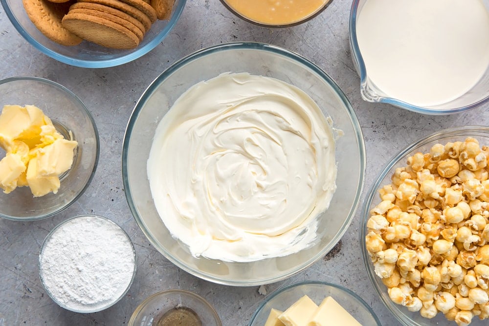 beaten cream cheese in a clear bowl surrounded by ingredients.